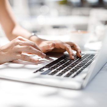 Hands of unrecognisable businesswoman typing on her laptop at cafe.